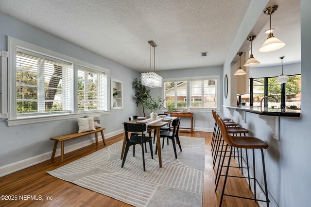 dining area featuring a textured ceiling, visible vents, wood finished floors, and baseboards