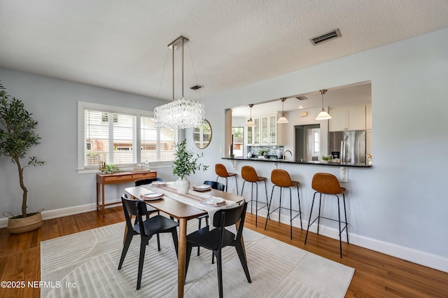 dining area featuring an inviting chandelier, visible vents, wood finished floors, and baseboards