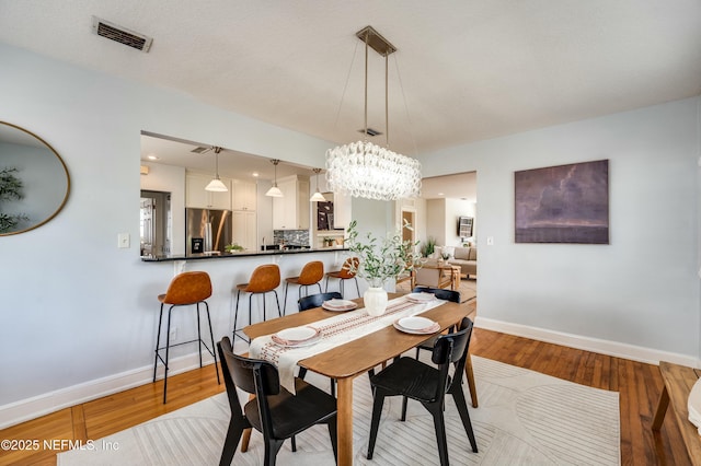 dining area with visible vents, wood finished floors, a chandelier, and baseboards