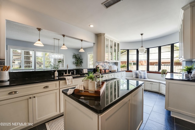 kitchen featuring a sink, glass insert cabinets, visible vents, a kitchen island, and pendant lighting
