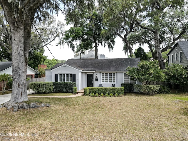 ranch-style house with a front yard, a shingled roof, stucco siding, and fence