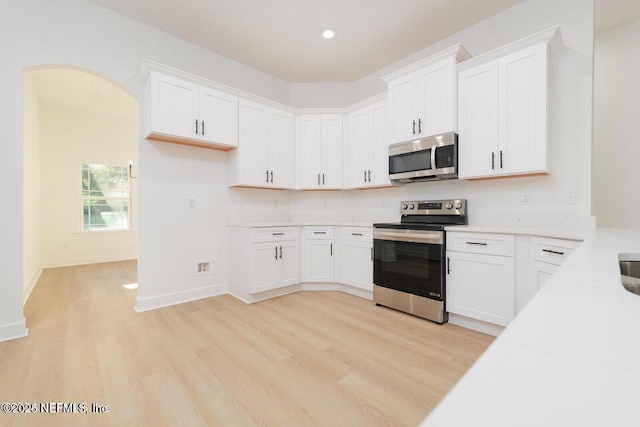 kitchen with light wood-type flooring, stainless steel appliances, light countertops, baseboards, and white cabinetry