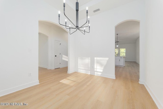 unfurnished dining area with visible vents, arched walkways, light wood-type flooring, baseboards, and a chandelier