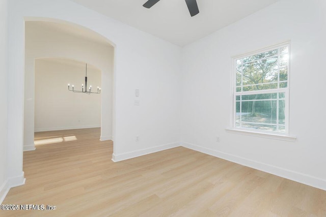 unfurnished room featuring ceiling fan with notable chandelier, light wood-style flooring, baseboards, and arched walkways