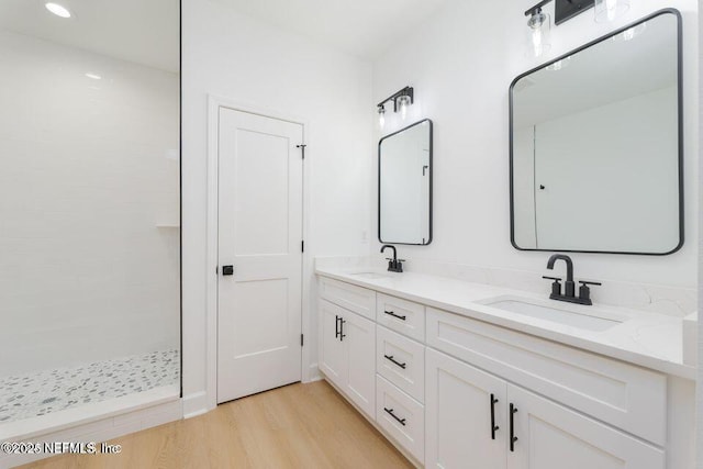 full bath featuring wood finished floors, a sink, double vanity, and tiled shower