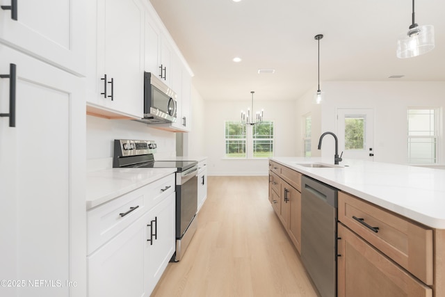 295 SE 57th St, Keystone Heights, FL 32656 - kitchen featuring appliances with stainless steel finishes, a sink, light wood finished floors, a chandelier, and white cabinetry