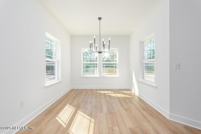 unfurnished dining area featuring baseboards, a notable chandelier, light wood-style floors, and a healthy amount of sunlight