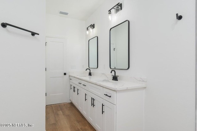 bathroom featuring wood finished floors, visible vents, a sink, and double vanity