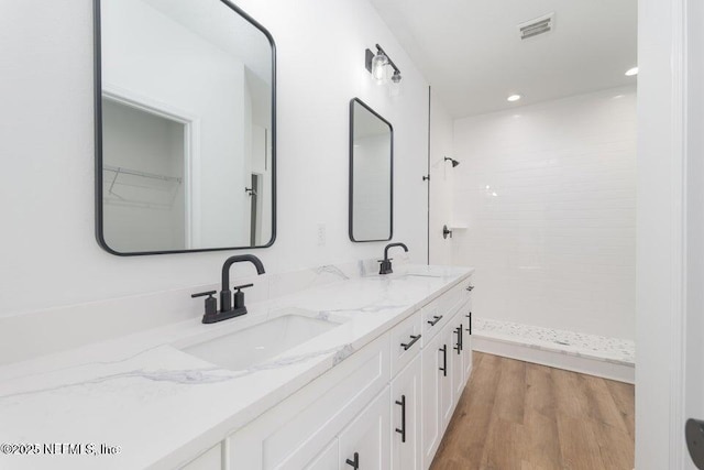 full bathroom with a tile shower, a sink, visible vents, and double vanity