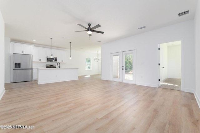 unfurnished living room featuring ceiling fan with notable chandelier, light wood-style flooring, visible vents, and a sink