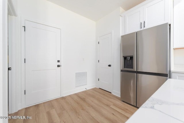 kitchen with white cabinets, light wood-style flooring, visible vents, and stainless steel fridge with ice dispenser