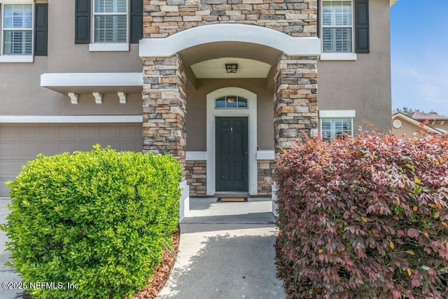 entrance to property with stone siding, stucco siding, and an attached garage