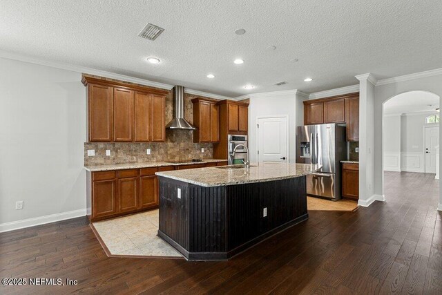 kitchen with appliances with stainless steel finishes, wall chimney range hood, arched walkways, hardwood / wood-style floors, and a sink