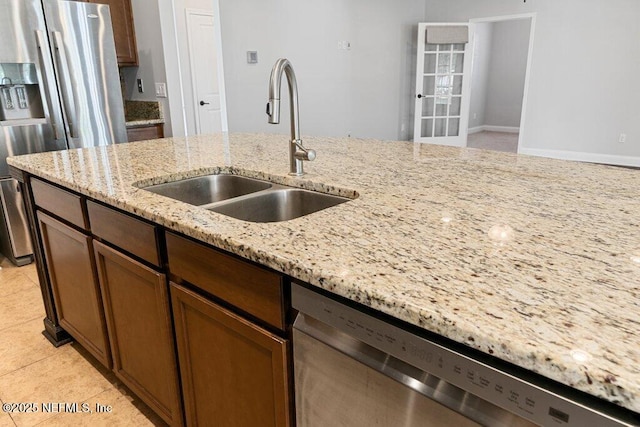 kitchen with appliances with stainless steel finishes, a sink, light stone countertops, and light tile patterned flooring