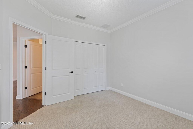 unfurnished bedroom with crown molding, carpet, a closet, baseboards, and a textured ceiling