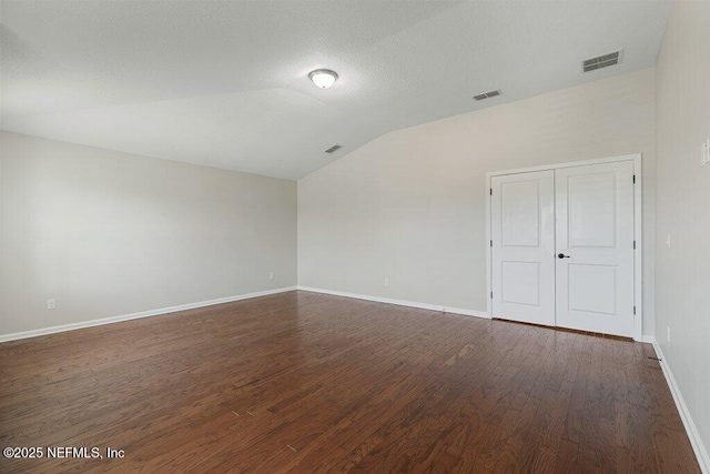 empty room featuring vaulted ceiling, dark wood-type flooring, and baseboards