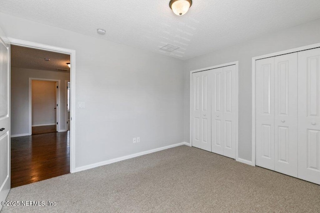 unfurnished bedroom with carpet, multiple closets, a textured ceiling, and baseboards