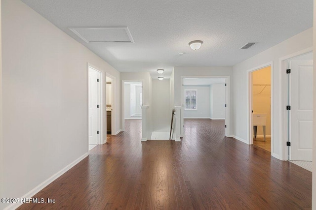 empty room with dark wood-style floors, baseboards, a textured ceiling, and attic access