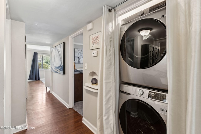 washroom featuring baseboards, dark wood-style flooring, stacked washer / drying machine, and laundry area