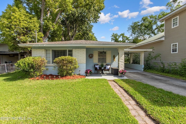 back of house with covered porch, fence, aphalt driveway, an attached carport, and a lawn