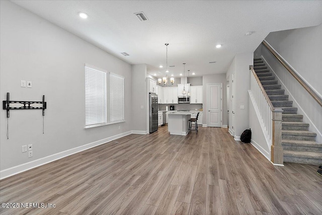 kitchen featuring wood finished floors, a kitchen island, a kitchen breakfast bar, appliances with stainless steel finishes, and a notable chandelier