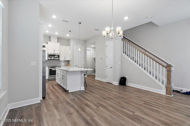kitchen with a kitchen island, a kitchen bar, appliances with stainless steel finishes, wood finished floors, and white cabinets