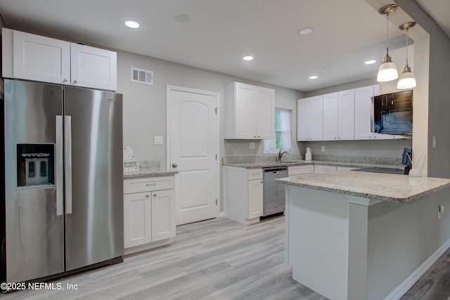 kitchen with white cabinetry, a sink, appliances with stainless steel finishes, light stone countertops, and a peninsula