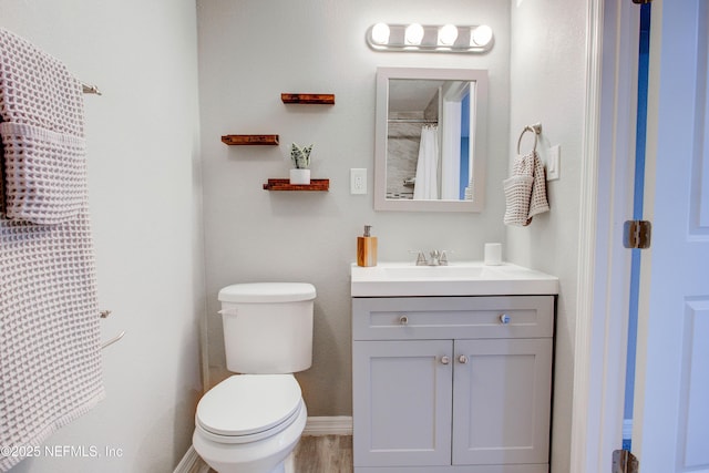 full bathroom featuring baseboards, wood finished floors, toilet, and vanity