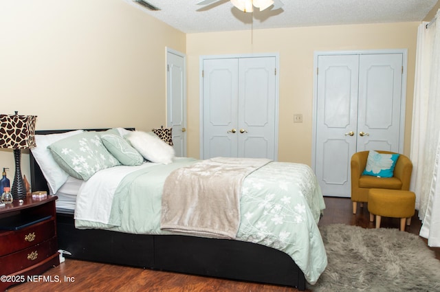 bedroom featuring wood finished floors, two closets, ceiling fan, visible vents, and a textured ceiling