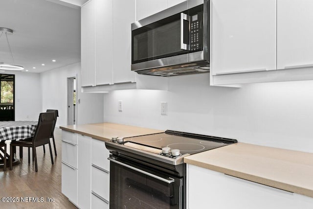 kitchen with light countertops, black electric range, white cabinetry, stainless steel microwave, and wood finished floors