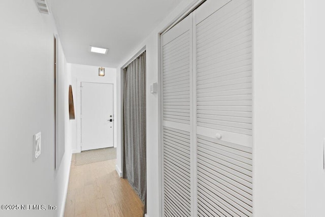 hall with light wood-style floors, baseboards, and visible vents