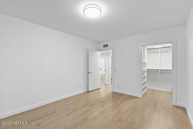 unfurnished bedroom featuring a walk in closet, visible vents, baseboards, a closet, and light wood-style floors