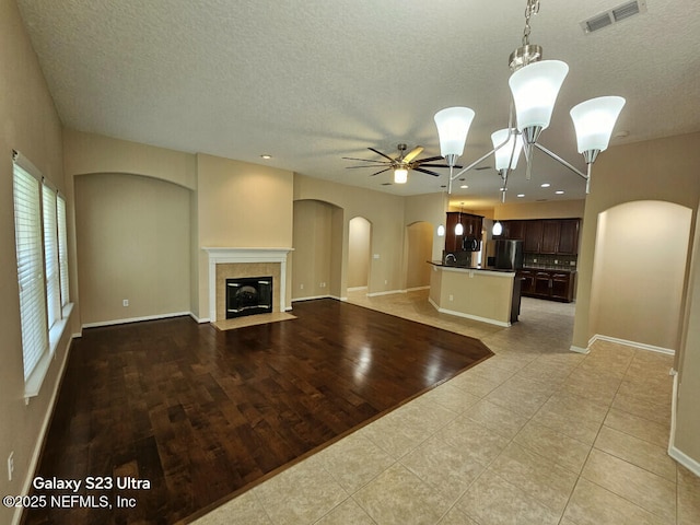 unfurnished living room featuring visible vents, arched walkways, a textured ceiling, and ceiling fan