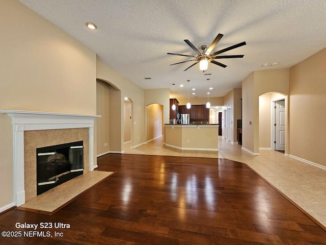 unfurnished living room with arched walkways, a textured ceiling, light wood-type flooring, ceiling fan, and a high end fireplace