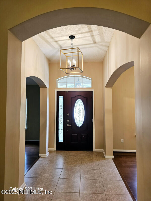 foyer entrance with tile patterned floors, a textured ceiling, arched walkways, baseboards, and a chandelier