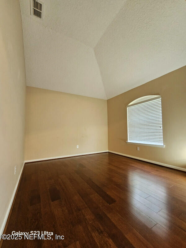 unfurnished room with wood-type flooring, vaulted ceiling, visible vents, and baseboards
