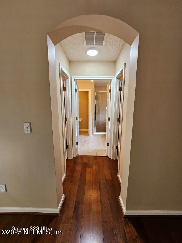 hall featuring arched walkways, baseboards, visible vents, and dark wood-style floors
