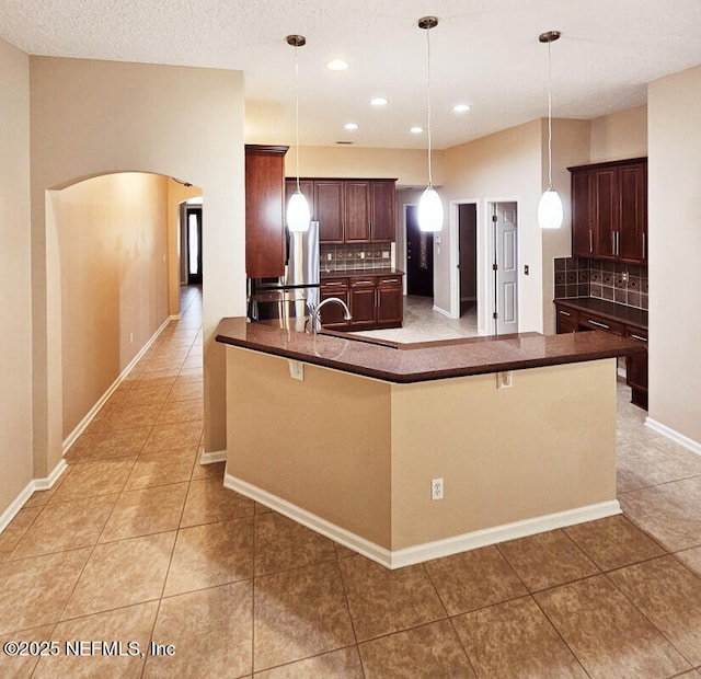 kitchen with dark countertops, tasteful backsplash, light tile patterned floors, arched walkways, and freestanding refrigerator