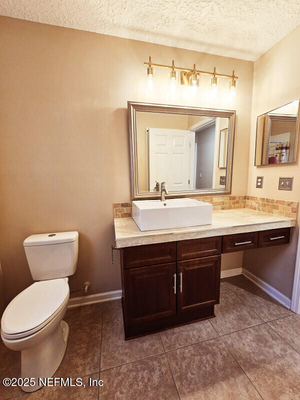 bathroom with a textured ceiling, toilet, vanity, and tile patterned floors
