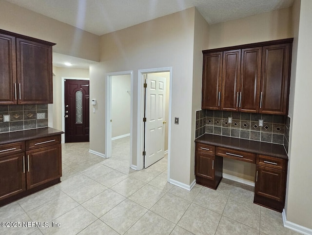 kitchen featuring backsplash, dark countertops, dark brown cabinetry, and light tile patterned floors
