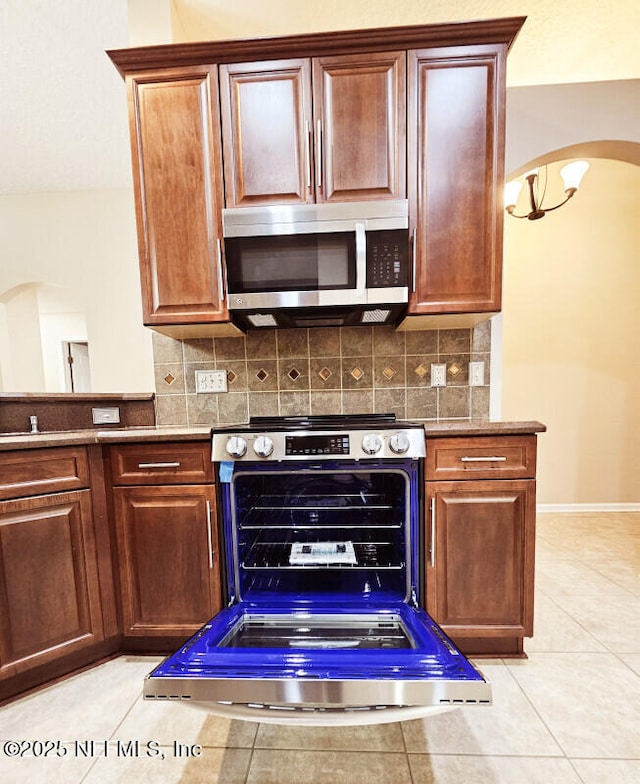 kitchen with arched walkways, backsplash, baseboards, and stainless steel appliances