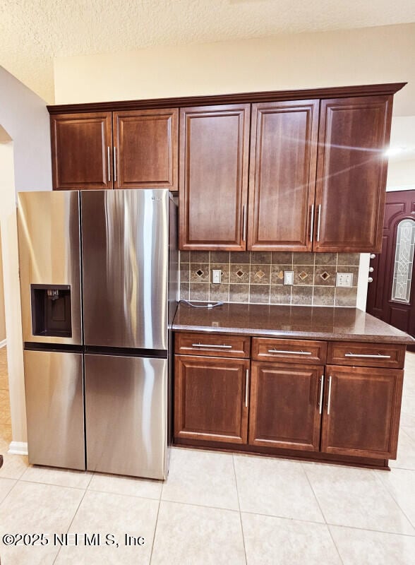 kitchen with dark stone counters, stainless steel fridge with ice dispenser, tasteful backsplash, and light tile patterned floors