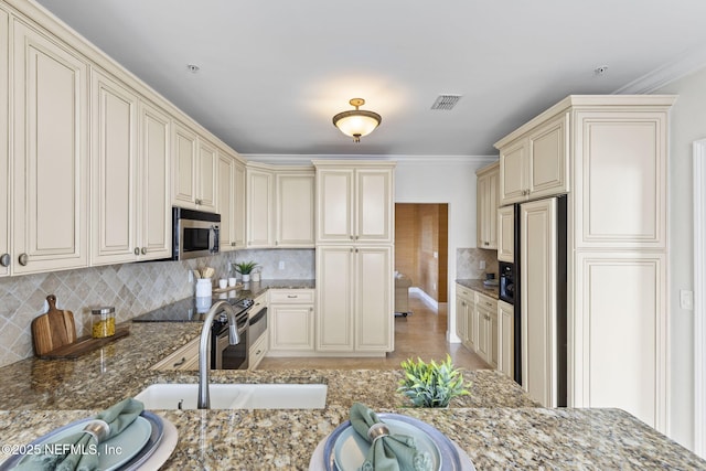 kitchen featuring paneled refrigerator, backsplash, a sink, stainless steel microwave, and cream cabinetry