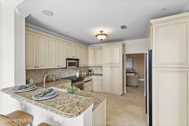 kitchen with visible vents, light stone countertops, a peninsula, stainless steel appliances, and cream cabinetry
