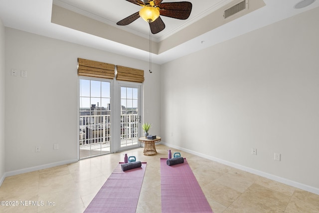 exercise area featuring a ceiling fan, a tray ceiling, ornamental molding, and baseboards