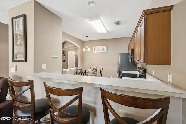 kitchen featuring a textured ceiling, appliances with stainless steel finishes, arched walkways, a peninsula, and brown cabinetry
