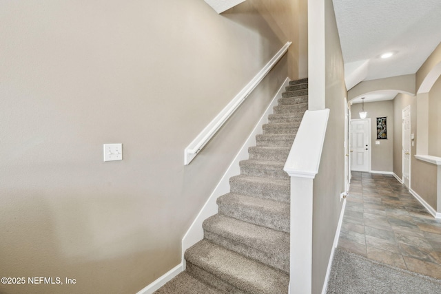 stairway with baseboards, stone finish flooring, arched walkways, and recessed lighting