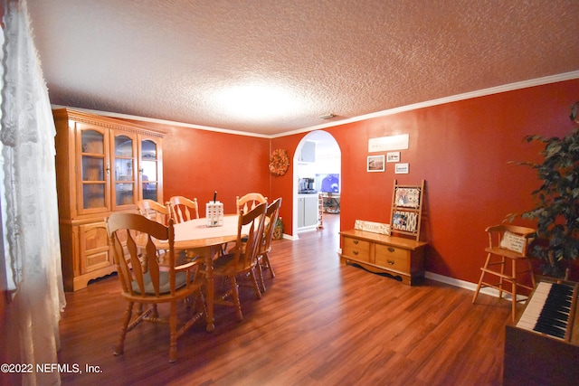 dining room featuring arched walkways, a textured ceiling, wood finished floors, and crown molding