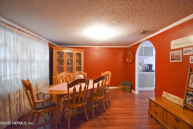 dining room featuring wood finished floors, crown molding, visible vents, and arched walkways