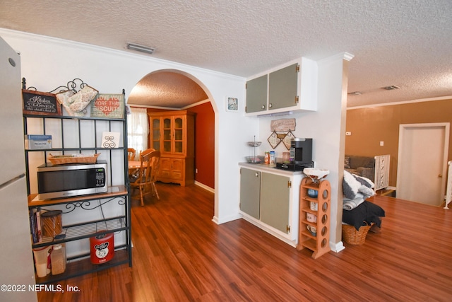 kitchen with arched walkways, wood finished floors, stainless steel microwave, a textured ceiling, and crown molding